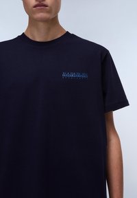T-shirt en coton bleu navy avec un col rond, coupe ample, présentant un petit logo bleu clair sur le côté gauche de la poitrine.