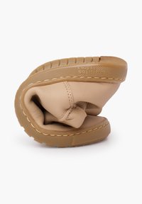 Beżowy skórzany but, zgięty, aby pokazać miękką cholewkę i teksturowaną gumową podeszwę. Widoczne detale przeszyć na cholewce i podeszwie.