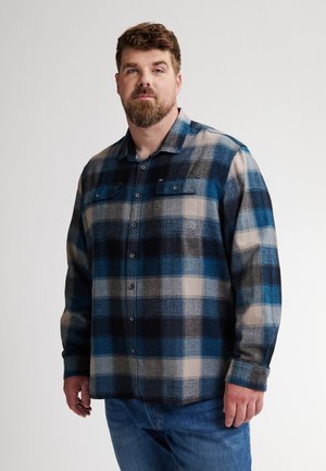 Camisa de franela con un patrón de cuadros en azul, gris y beige. Presenta un cierre de botones y dos bolsillos en el pecho. Textura suave, mangas largas.