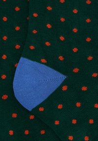 Calzini verdi con pois arancioni. Presentano un'area del tallone blu. Realizzati in tessuto morbido con una texture a maglia fine.