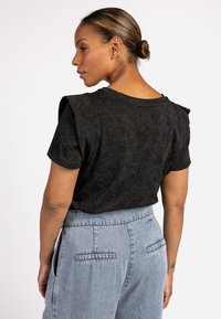 Zwarte, textuur geprinte t-shirt met korte mouwen en schouderaccenten, gecombineerd met lichtblauwe denim high-waisted broek met achterzakken.