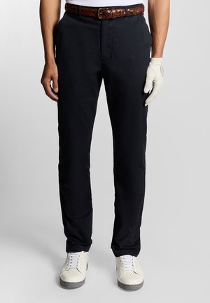 Black trousers with a flat front and side pockets, paired with a braided brown leather belt. Worn with a white shirt and gloves.