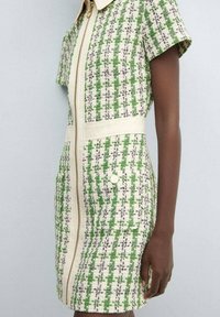 Abito a motivi verdi e bianchi con maniche corte, chiusura con zip e dettagli color crema, dotato di tasche e scollo con colletto.