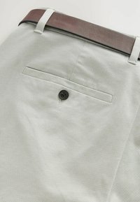 Pantalones gris claro con un patrón y un acabado texturizado, que cuentan con un bolsillo trasero con un botón negro y un cinturón marrón.