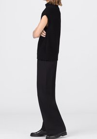 Svart ärmlös polotröja med ribbstruktur, i kombination med vida svarta byxor och svarta boots i ankellängd.