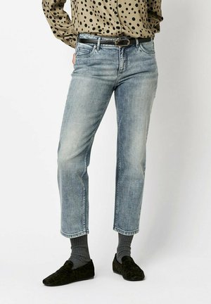 Light blue denim jeans with a straight-cut design, faded finish, five-pocket style, and a black belt. Worn with a patterned blouse and dark shoes.