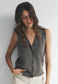 Šedý bezrukávový cardigan s výstrihom do V, textúrovanou pleteninou a šiestimi tmavými gombíkmi na prednej strane. Svetlé pozadie.