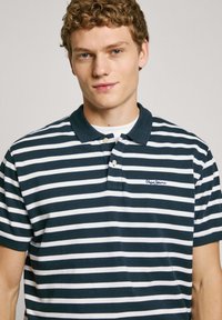 Navy and white striped polo shirt with a collar, short sleeves, and embroidered logo. Made of textured cotton fabric. Buttons on the placket.