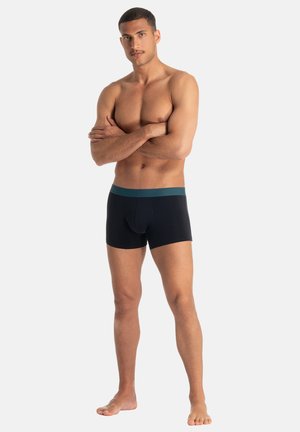 Boxer neri con fascia in vita color teal, caratterizzati da una vestibilità aderente e una texture morbida, indossati da una persona in piedi con le braccia incrociate.