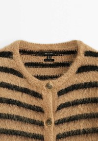 Cardigan beige en maille duveteuse avec des rayures horizontales noires, encolure ronde et deux boutons métalliques décoratifs sur le devant.
