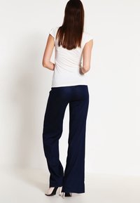 Námořnické široké kalhoty vyrobené z měkké látky, kombinované s vypasovaným bílým tričkem. Oblečení se vyznačuje hladkou texturou a minimalistickým designem.