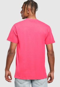 Camiseta de manga corta en algodón rosa brillante, con cuello redondo clásico y corte relajado, vista que muestra la parte trasera con detalles mínimos.