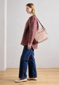 Maglione rosso con motivo, jeans blu a gamba larga e scarpe basse beige chiaro. Porta una borsa a tracolla rosa tenue con tracolla marrone.