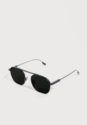 Black metal-framed sunglasses with thin arms and dark tinted lenses, resting on a white surface.
