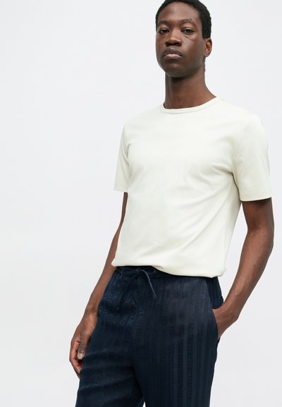 Helebeez lühikese varrukaga t-särk ümmarguse kaelusega, kombineeritud tumedate laevandustega pükstega, millel on vertikaalne triibuline tekstuur ja nöörivöö.