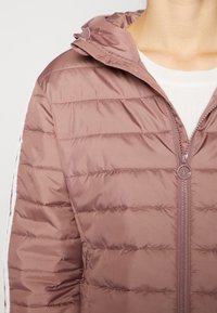 Brązowa kurtka puchowa z kapturem, pikowaną teksturą, przednim zamkiem błyskawicznym i białymi paskami po bokach. Wykonana z gładkiego, lekkiego materiału.