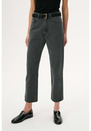 Osoba ubrana w ciemnoszare wysokiego stanu jeansy o prostych nogawkach z czarnym paskiem, czarny bezrękawnik i czarne skórzane mokasyny.