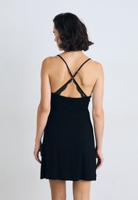 Zwarte jurk met een A-lijn silhouet, voorzien van dunne straps en kantdetails aan de achterkant. Zacht, glad materiaal met een comfortabele pasvorm.