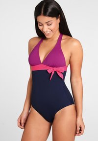 Eén stuk badpak met een paarse driehoekige top en een roze strikaccent bij de taille, met een blauwe onderkant. Soepele, rekbare stof.