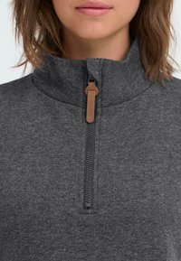 Grijze fleece pullover met rits en hoge kraag. Heeft een zwarte rits en een bruine trekhaak. Zachte textuur en eenvoudig ontwerp.
