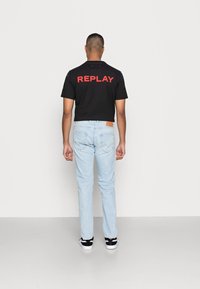 Svart kortärmad t-shirt med röd text "REPLAY" på ryggen, i kombination med ljusblå denimjeans och svartvita sneakers.