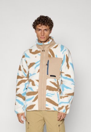 Giacca in pile con un motivo camouflage bianco, marrone e azzurro chiaro, caratterizzata da un colletto alto e una tasca sul petto con zip di colore beige.
