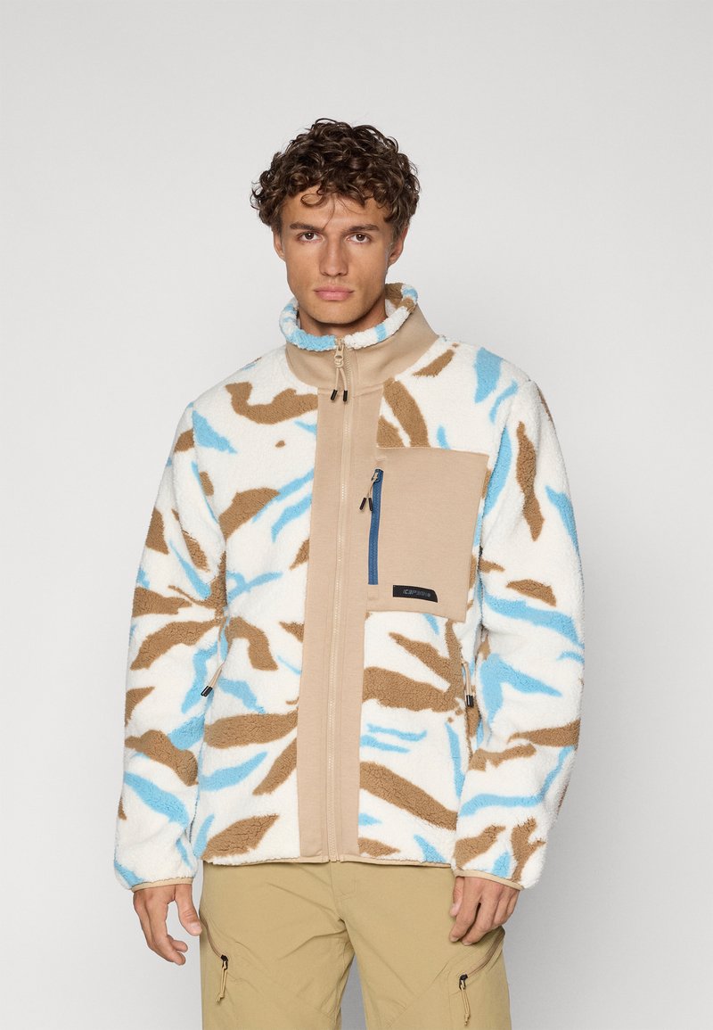 Giacca in pile con un motivo camouflage bianco, marrone e azzurro chiaro, caratterizzata da un colletto alto e una tasca sul petto con zip di colore beige.