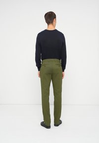Olive green spodnie z dwiema tylnymi kieszeniami, noszone z granatową koszulą z długim rękawem. Prosty krój i teksturowana tkanina, widziane z tyłu.
