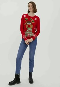 Czerwony sweter z motywem renifera z dużym nosem, noszącego zielony szalik. Dodatki obejmują płatki śniegu i wzór z dzianiny. Noszony z niebieskimi dżinsami.