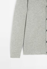 Manche et côté de cardigan en maille côtelée gris clair avec boutons noirs sur fond blanc.