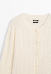 Cardigan en laine couleur crème avec motif torsadé et col rond, fermé devant par des boutons assortis.