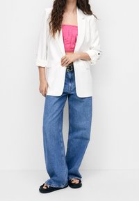 Weißer Oversized-Blazer, pinkes Crop-Top, hoch geschnittene blaue Jeans und schwarze Sandalen. Glattes Material, lockere Passform, weit geschnittene Hosenbeine.