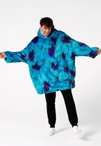 Mėlynas oversize stiliaus džemperis su violetinėmis ir juodomis raižytomis dėmėmis. Minkšta, pūkuota medžiaga su plačiomis rankovėmis ir priekinių kišenių. Patogus prigludimas.