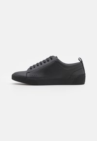 Schwarze Sneakers mit Obermaterial aus strukturiertem Leder, runder Zehenpartie und flacher Gummisohle. Verfügt über sechs Ösen und einen Zugriegel an der Ferse.