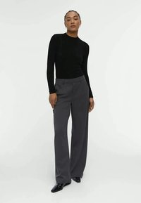 Black ribbed long-sleeve top paired with gray tailored trousers. The trousers have a straight-leg cut and are made from a smooth fabric.