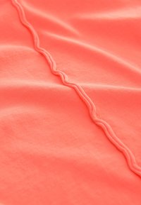 Tessuto corallo con una consistenza liscia presenta una cucitura ondulata che scorre verticalmente al centro, evidenziando il suo colore brillante e il design.