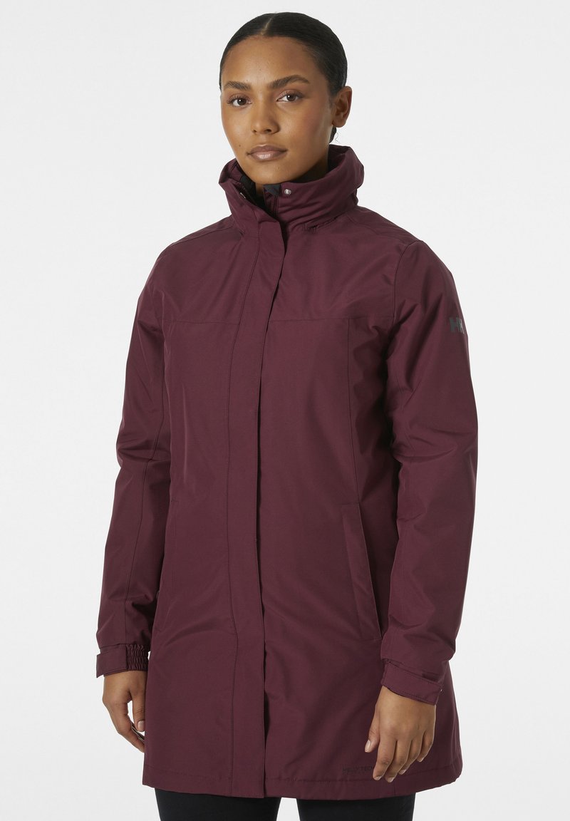 Chaqueta impermeable de color marrón con cuello alto, cremallera frontal y puños elásticos. Cuenta con dos bolsillos laterales y un discreto logo de la marca en la manga.