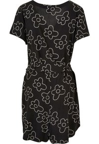 Combinaison noire à manches courtes avec de grands motifs floraux blancs en contour et une ceinture cintrée à la taille.