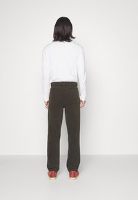 Hnědé manšestrové kalhoty s volnějším střihem, vysokým pasem a dvěma zadními kapsami, doplněné o jednobarevnou bílou košili s dlouhým rukávem a červenými botami.