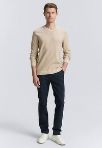 Beige v-ringad tröja med texturerad yta, kombinerad med mörkblå byxor och vita sneakers, vilket skapar en avslappnad outfit för män.