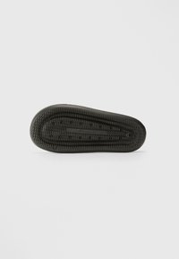Svart gummisåle med en teksturert overflate. Har et sirkulært mønster og en sentral hevet stripe for bedre grep.