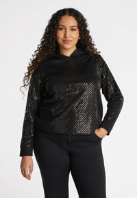 Felpa nera con cappuccio caratterizzata da un motivo a righe diagonali in paillettes. Presenta maniche lunghe e una vestibilità morbida, abbinata a pantaloni neri.