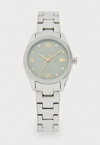 Relógio de pulso em metal prateado com caixa redonda, mostrador verde, índices horários em ouro e bezel texturizado. Inclui uma bracelete de metal com elos e detalhe do logo.