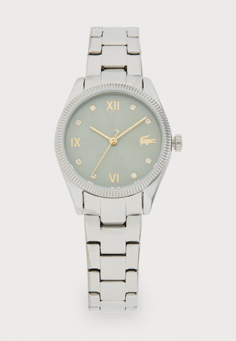 Relógio de pulso em metal prateado com caixa redonda, mostrador verde, índices horários em ouro e bezel texturizado. Inclui uma bracelete de metal com elos e detalhe do logo.