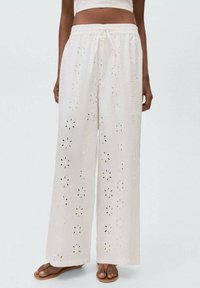Pantaloni albi cu picioare largi, confectionati dintr-un material brodat, cu modele florale decupate, talie elastica si sireturi.