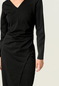 Vestido negro de manga larga con un escote en V profundo, que presenta una silueta ajustada y un diseño drapeado en la cintura, fabricado con un tejido suave.