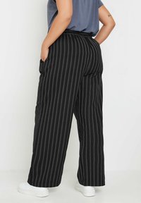 Pantaloni a gamba larga a righe nere con un tessuto testurizzato, dotati di una vita alta e tasche laterali, abbinati a sneakers bianche.