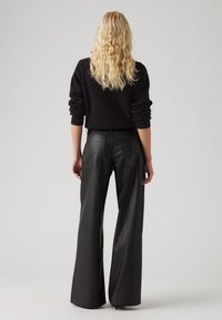 Czarne szerokie spodnie z skóry z gładką fakturą i tylnymi kieszeniami, w połączeniu z ciemnym, teksturowanym swetrem w luźnym kroju.