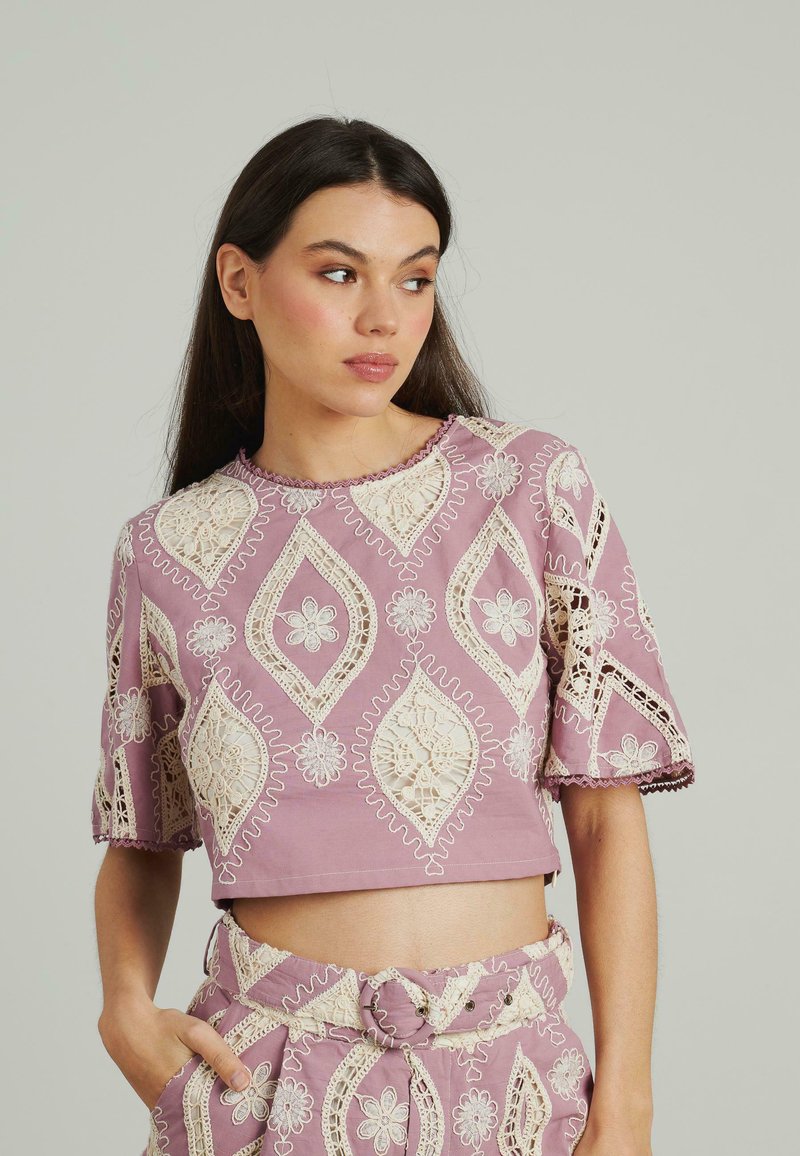 Lila Cropped-Top mit aufwendiger cremefarbener Spitze in Diamant- und Blumenmustern, kurzen Ärmeln und gewellten Kanten.