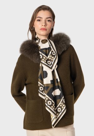 Olijfgroen gebreid sweater met een nepbont kraag, gecombineerd met een crèmekleurige zijden sjaal met geometrische bruine en zwarte patronen.